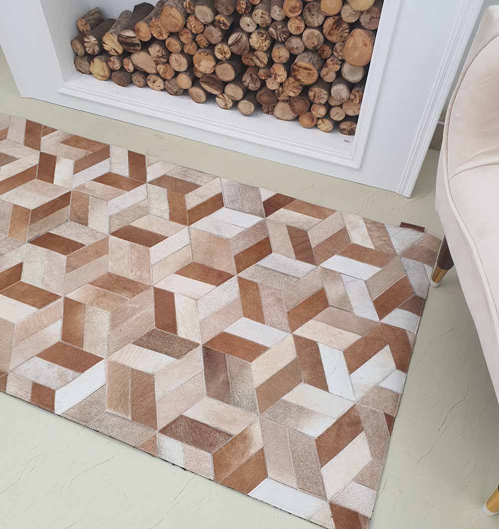 The RAMSHA HOME Geometric Cube Pattern Handmade Leather Area Rug LR-012, featuring brown, beige, and white 3D cubes, is placed before a log-filled fireplace. A cream chair appears on the right.