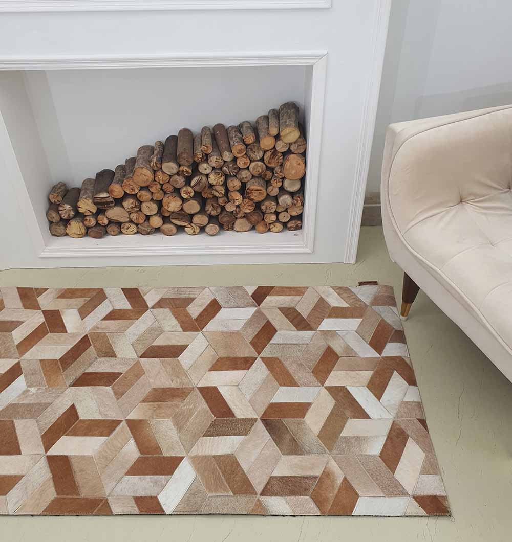 The RAMSHA HOME Geometric Cube Pattern Handmade Leather Area Rug LR-012 in brown, beige, and white is placed beside a cream armchair and a stack of firewood arranged in a white fireplace niche.