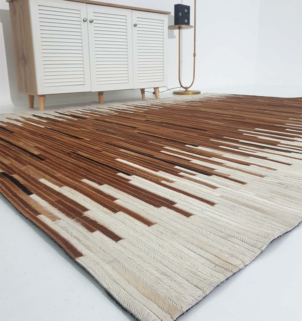 The RAMSHA HOME Handmade Multi-Color Leather and Wool Area Rug LR-014 adds style in brown and beige tones in front of a white cabinet with wooden legs, with a tall lamp positioned nearby against the white wall.