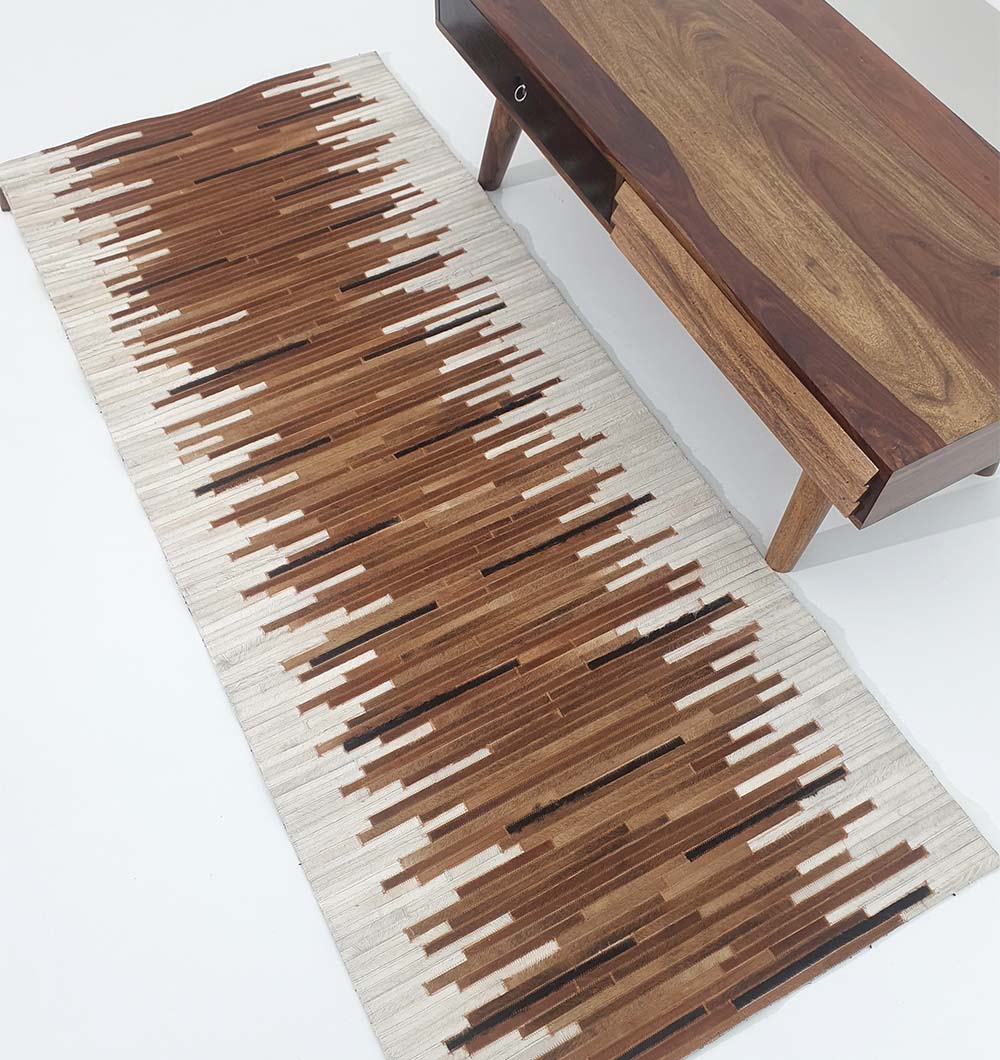 A wooden table with angled legs sits beside the RAMSHA HOME Handmade Multi-Color Leather and Wool Area Rug LR-014, featuring brown and beige vertical stripes that gently fade at the edges, on a white floor.