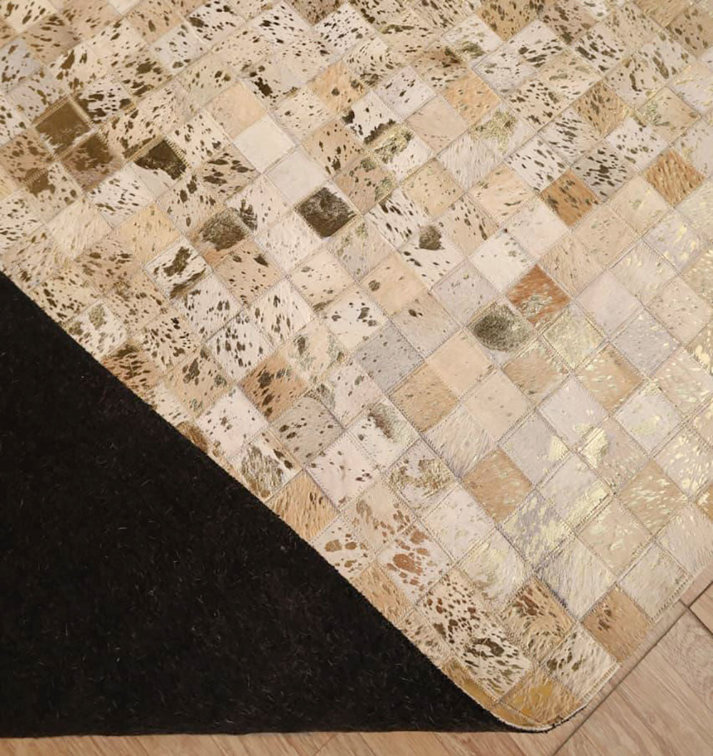 A close-up of the RAMSHA HOME Handmade Mosaic Patchwork Beige & Tan Leather Rug LR-015 shows its small square tiles, a folded corner revealing a dark backing, and the rug placed on a wooden floor.