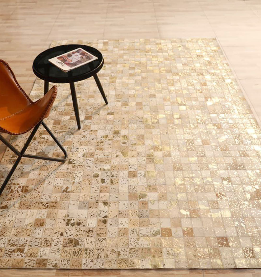 A brown leather chair and a round black side table with a magazine sit atop the RAMSHA HOME Handmade Mosaic Patchwork Beige & Tan Leather Rug LR-015, placed over a light wooden floor.