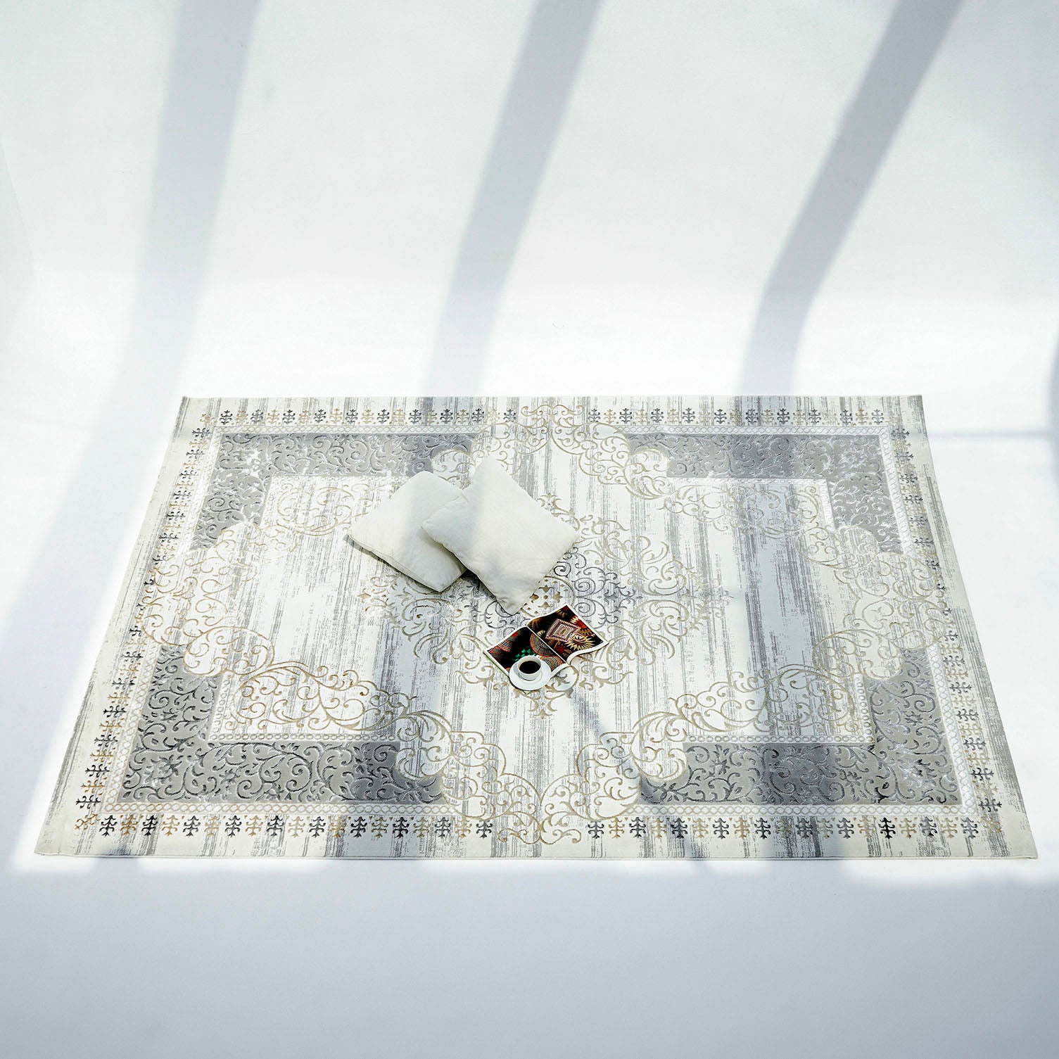 The RAMSHA HOME Light Grey Color NK36B 100% Polyester Silk Rug is paired with two white cushions and a tray of coffee and snacks, all arranged beneath the gentle shadows of tree branches.