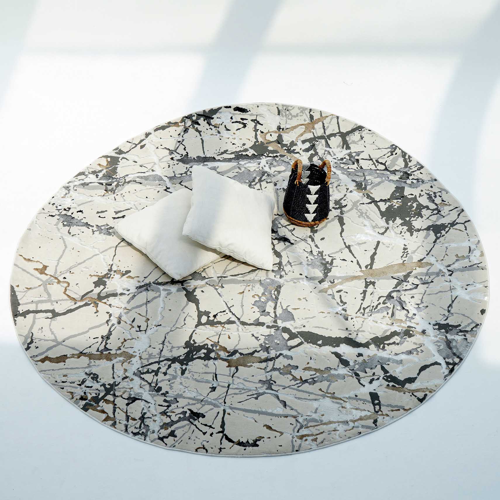 The RAMSHA HOME Machine Made Turkey Carpet MZ29C features a cream base with abstract gray, beige, and black splatters. Two white pillows and a geometric woven basket rest on this polyester rug as sunlight casts soft shadows across the floor.