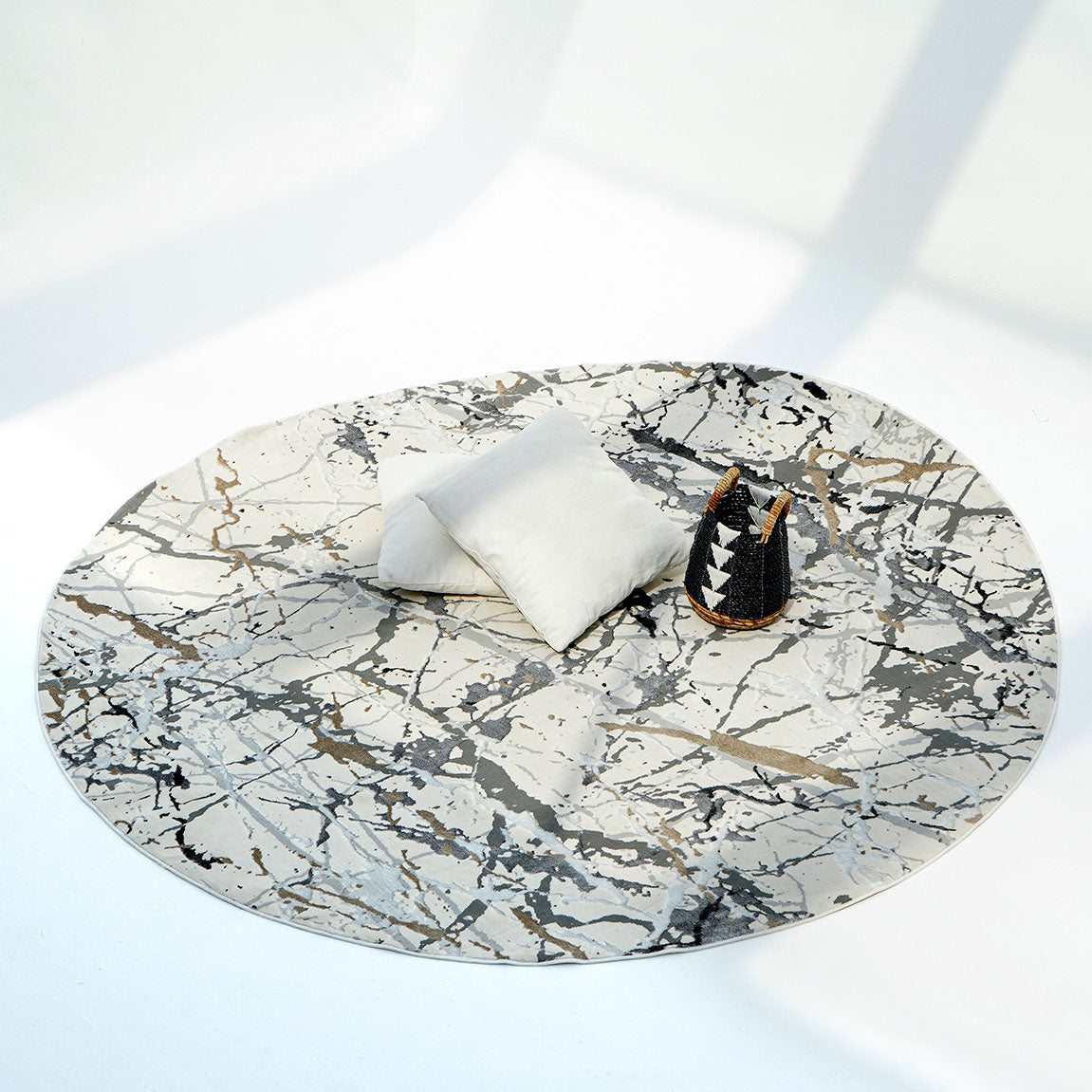 The RAMSHA HOME Machine Made Turkey Carpet Cream Colored MZ29C features a marble look with white, black, and gray lines. It rests on a white floor, accented by two white cushions and a small woven basket under natural light.