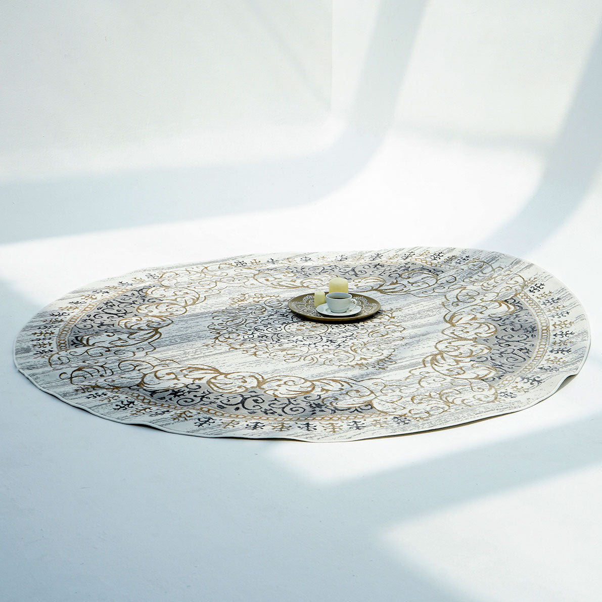The RAMSHA HOME Light Grey Color NK36B 100% Polyester Silk Rug with ornate floral patterns lies on a white floor, with a small tray holding a white cup and saucer at its center, as soft shadows fall across the scene.