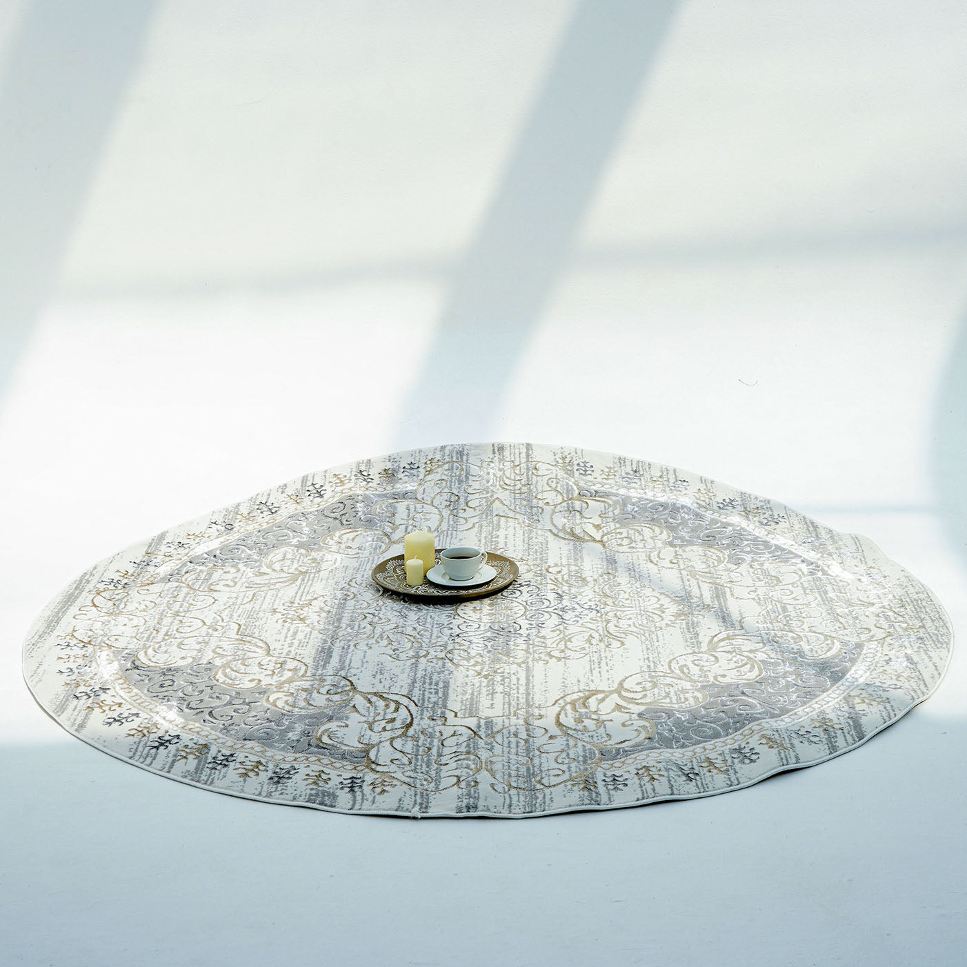 The RAMSHA HOME Light Grey Color NK36B 100% Polyester Silk Rug rests on a white floor, accented with a small tray holding a cup, saucer, and two candles at its center as light and shadows dance across the scene.