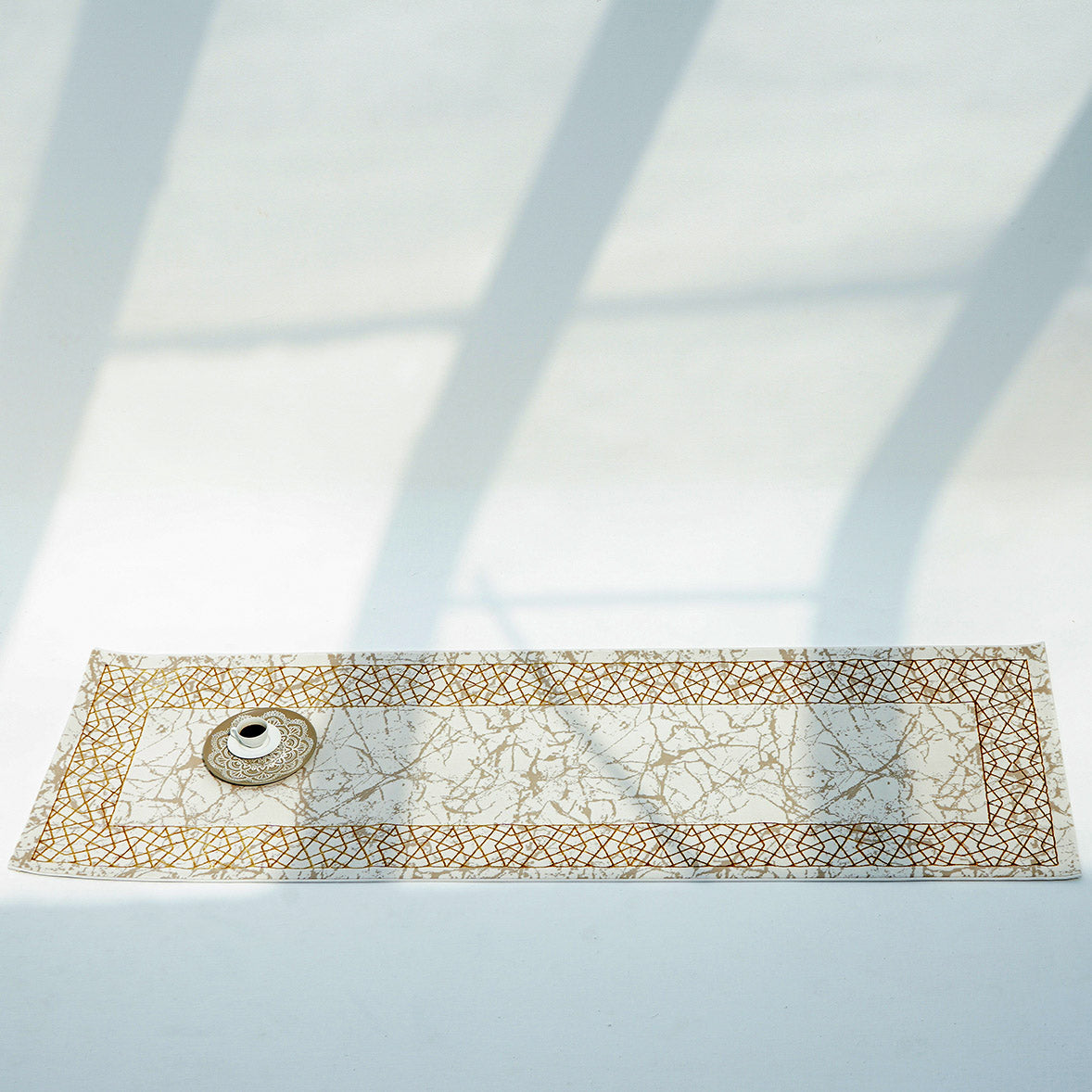 The RAMSHA HOME Cream, Shrink Cream Colored Geometry Pattern Turkey Rug MZ67C features delicate gold geometric borders and a white pattern, lying on a white surface with a ceramic bowl and plate atop, casting elegant shadows.
