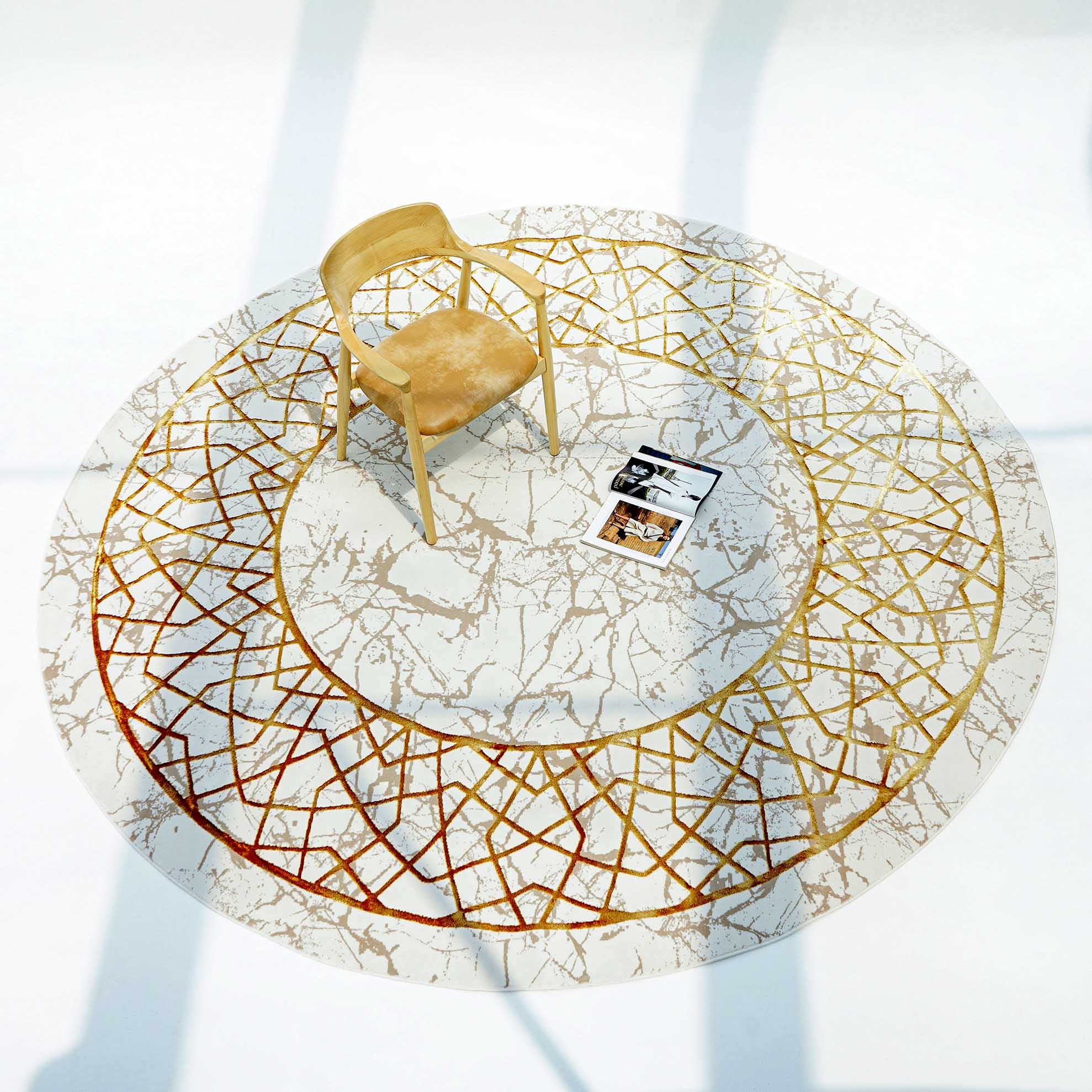 A wooden chair sits on the RAMSHA HOME Cream, Shrink Cream Colored Geometry Pattern Turkey Rug MZ67C, its modern cream and ivory tones accented by gold and bronze lines. Two magazines lie nearby, all illuminated by bright natural light.