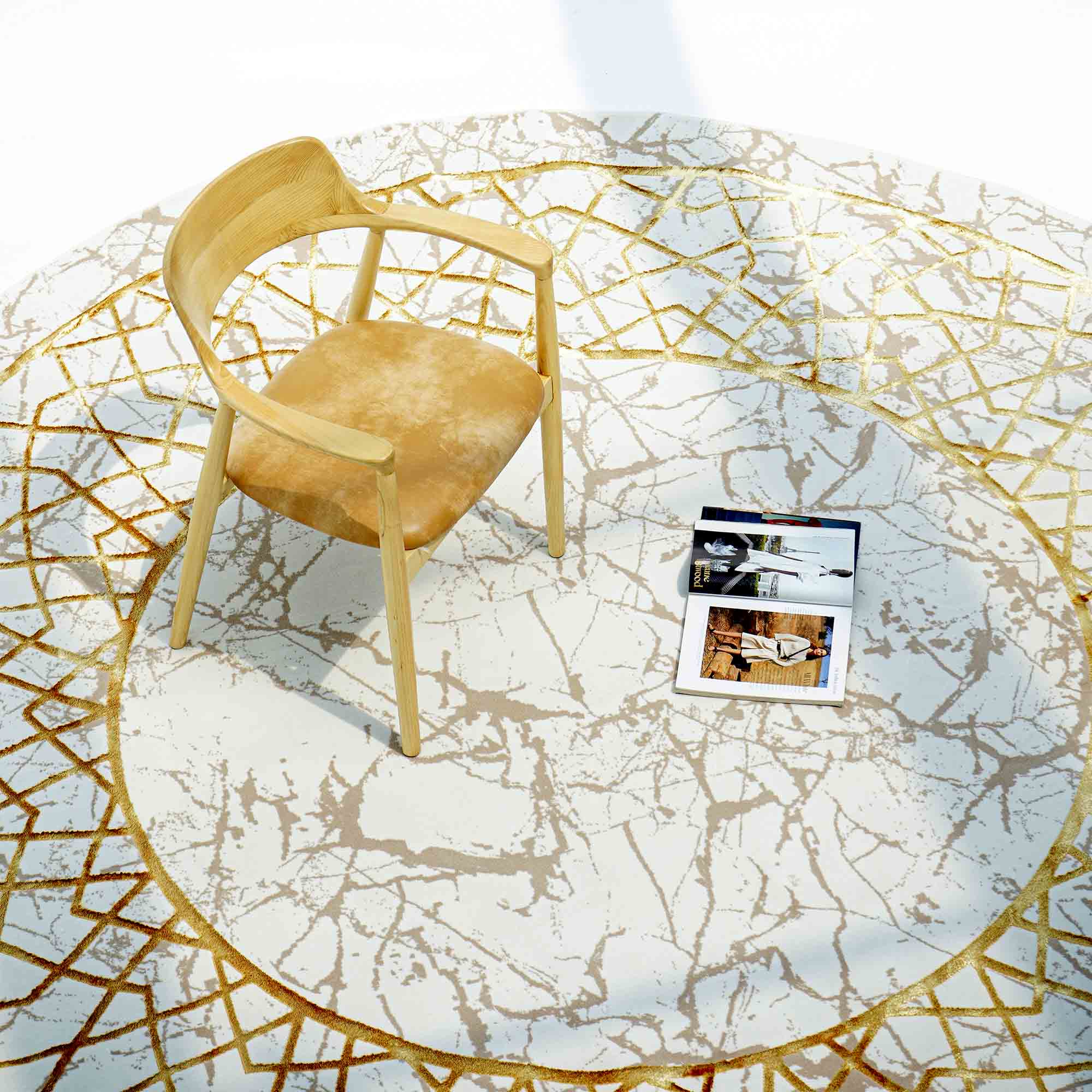 A light wooden chair with a tan seat sits on a RAMSHA HOME Cream, Shrink Cream Colored Geometry Pattern Turkey Rug (MZ67C), with two open interior design magazines placed on the rug in front of the chair.
