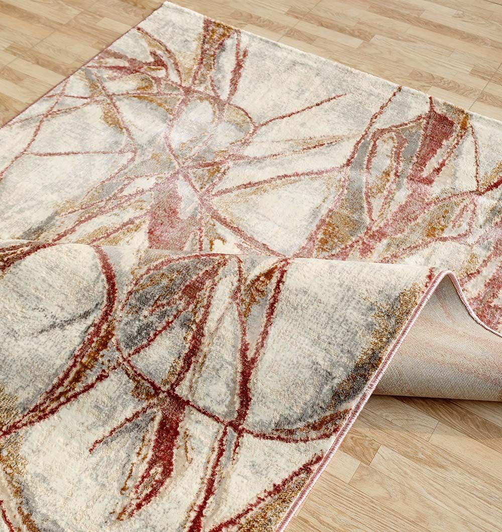 The Abstract Scribble Line Ivory Rug with Rust & Gold Accents (150x210 cm) by RAMSHA HOME features intersecting lines and soft blended colors, making it a modern choice for any space. It lies partially folded on a light wood floor.