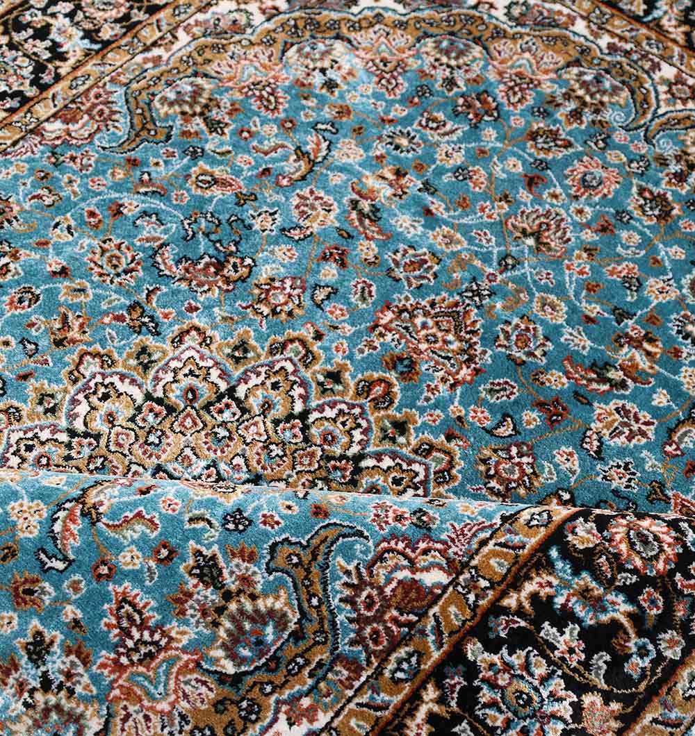A close-up of the RAMSHA HOME Persian Floral Medallion Teal Blue Rug (MMB 05, 150x210 cm), featuring red, cream, and brown floral motifs with a detailed black border and a slightly folded corner.