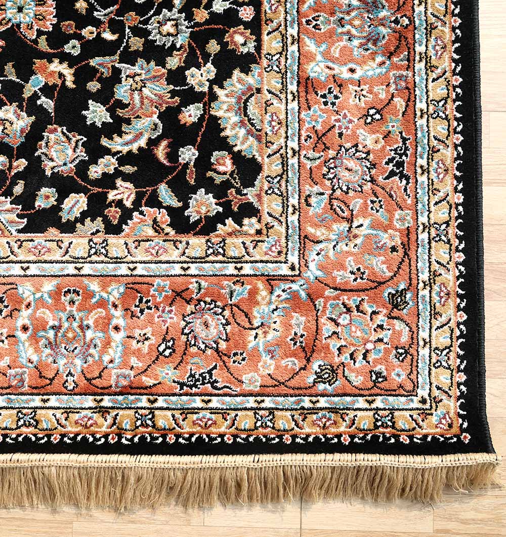 A close-up of the RAMSHA HOME Persian Floral Black Rug with Red Border – MMB 10 (175X275 cm) features a black center with floral motifs, a red border adorned with colorful designs, and beige fringe along the edge.