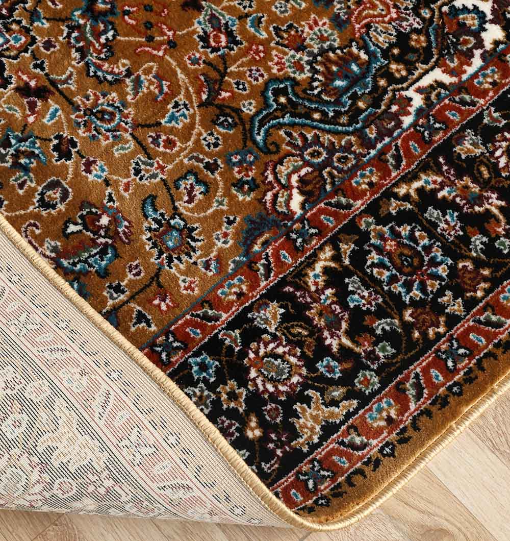 A close-up of the RAMSHA HOME Persian Floral Medallion Rust & Black Border Rug (MMB 15, 235x330 cm) shows its rich hues and a lifted corner revealing the woven underside and edge on a wooden floor.