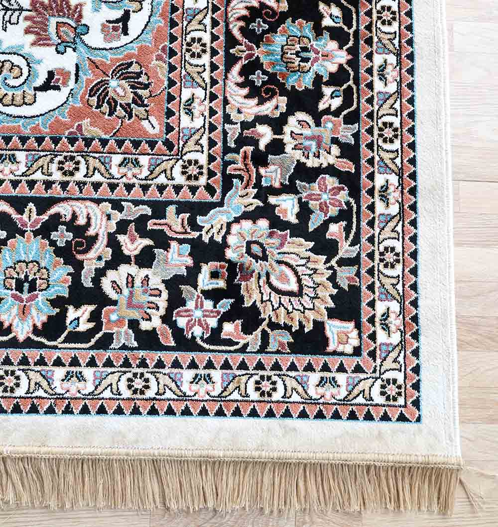 A close-up of the RAMSHA HOME Multi Color Decor Rug - MMB 20 (265X365 cm) shows its intricate blue, red, cream, and black floral patterns with a detailed border and beige fringes, set on a light wooden floor.