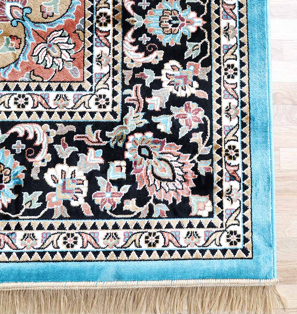Close-up of the RAMSHA HOME Multi Color Decor Turkish Area Rug (MMB 22, 265x365 cm), featuring intricate floral and geometric patterns in black, blue, pink, and cream with a light blue border and beige fringe on a wooden floor.