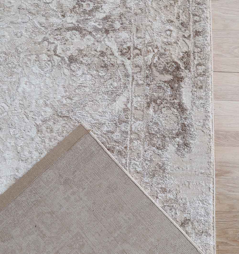 A close-up of the RAMSHA HOME Modern Multi Abstract Machine-Made Carpet - MMB 078 (180 x 270 cm) on a light wooden floor, with a corner flipped to reveal its solid beige underside and intricate abstract design.