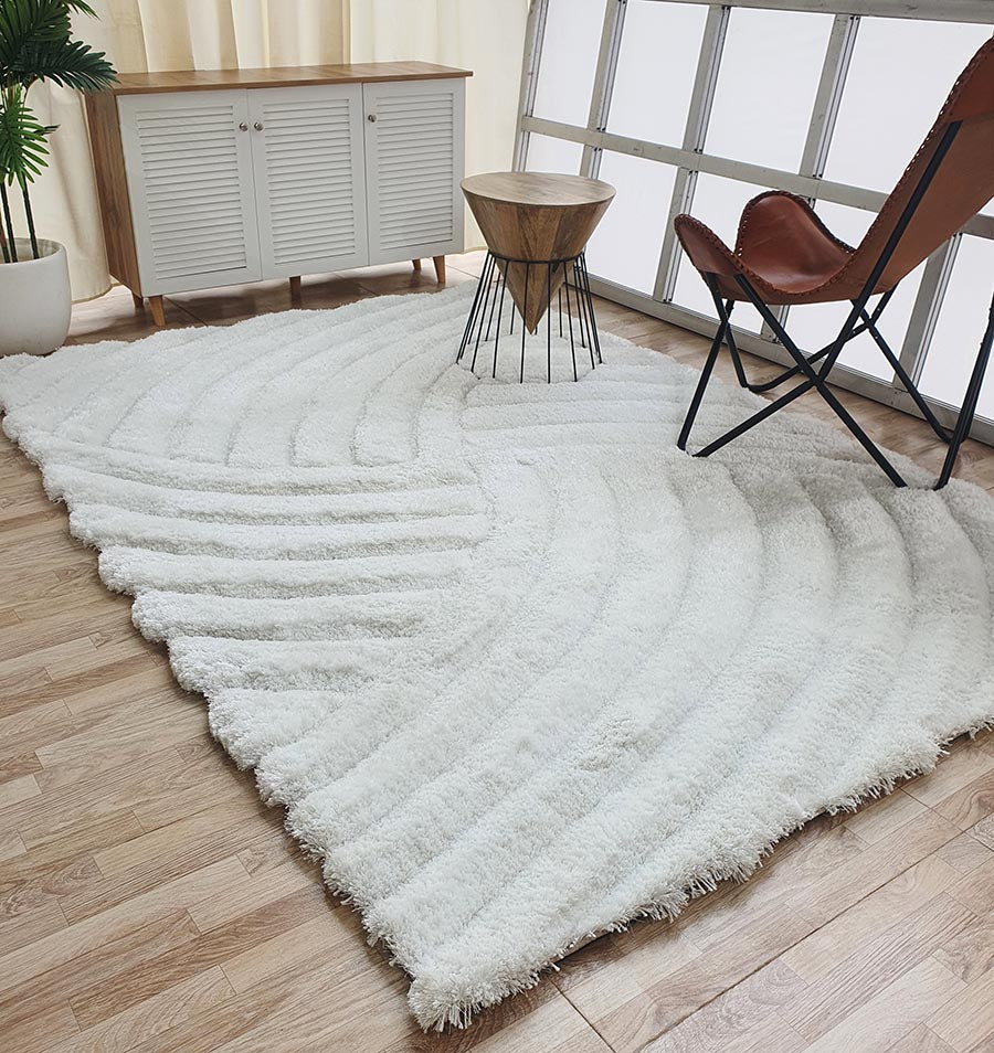 A modern living room with a RAMSHA HOME White Shaggy Area Rug for Large Living Room - MP3D 01, a small wooden table with metal legs, brown leather chair, white cabinet, and wood flooring bathed in natural light from large windows.