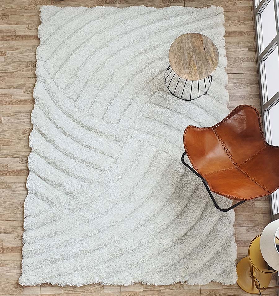 A RAMSHA HOME White Shaggy Area Rug for Large Living Room (MP3D 01) covers the wooden floor, with a round wood-top side table and a brown leather butterfly chair placed on it by large windows.