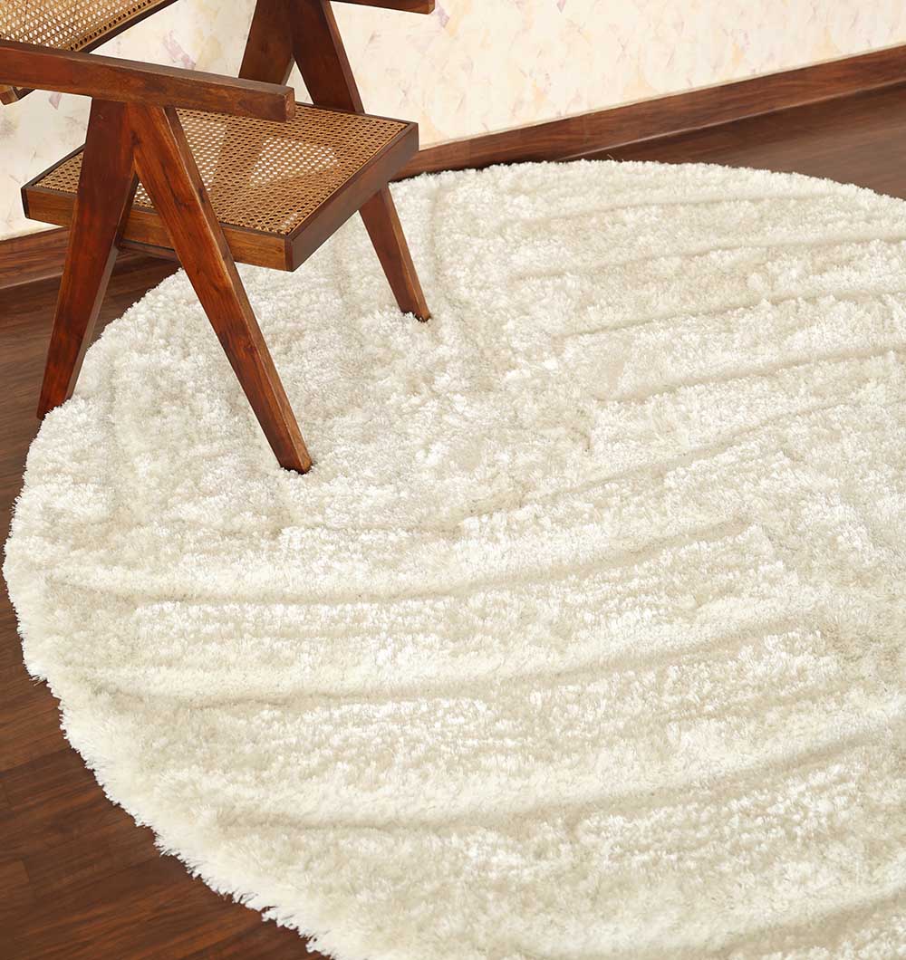 The RAMSHA HOME White Plush Round Shaggy Rug - MP3D 07 rests on a dark wooden floor, topped with a sleek wooden chair featuring a woven cane seat, placed near a wallpapered wall.