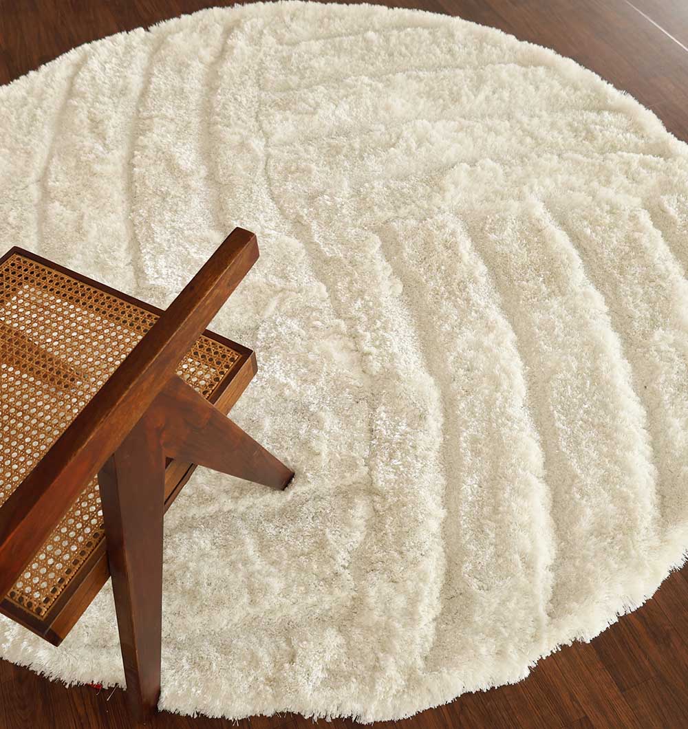 A RAMSHA HOME White Plush Round Shaggy Rug - MP3D 07 lies on a dark wooden floor, with a wooden chair featuring a woven cane seat and backrest partially visible in the corner.