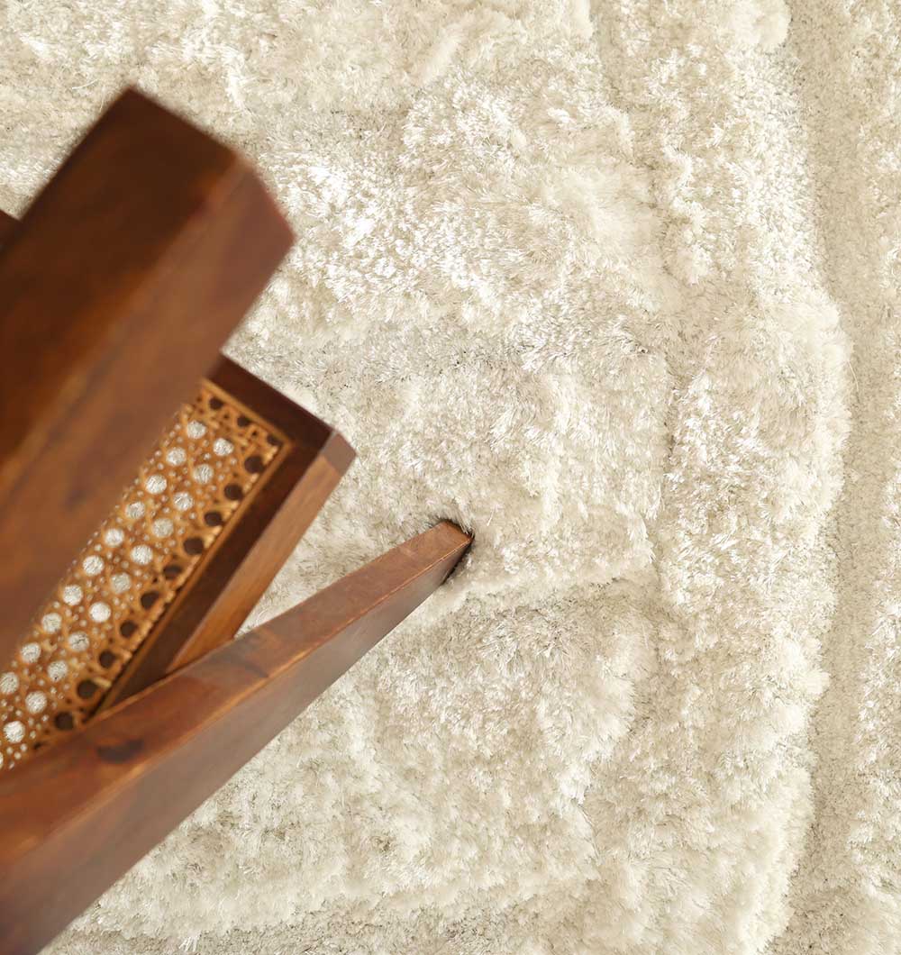 A close-up of a wooden chair with a woven cane backrest sits on the RAMSHA HOME White Plush Round Shaggy Rug - MP3D 07, adding warmth and comfort to the space.