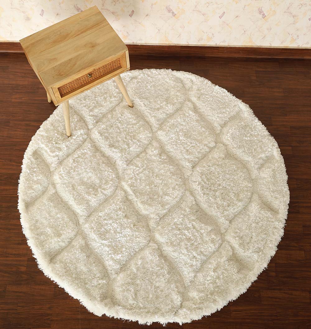 The RAMSHA HOME White Round Shaggy Rug with Carved Pattern - MP3D 13 sits on a dark wooden floor beside a small, light wood side table with woven detailing.