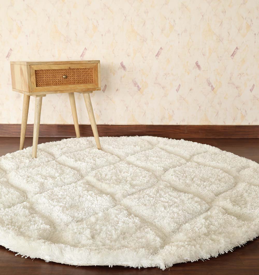 A White Round Shaggy Rug with Carved Pattern - MP3D 13 by RAMSHA HOME sits on a wooden floor beside a light wood mid-century modern nightstand with a cane drawer, set against a pale patterned wall.