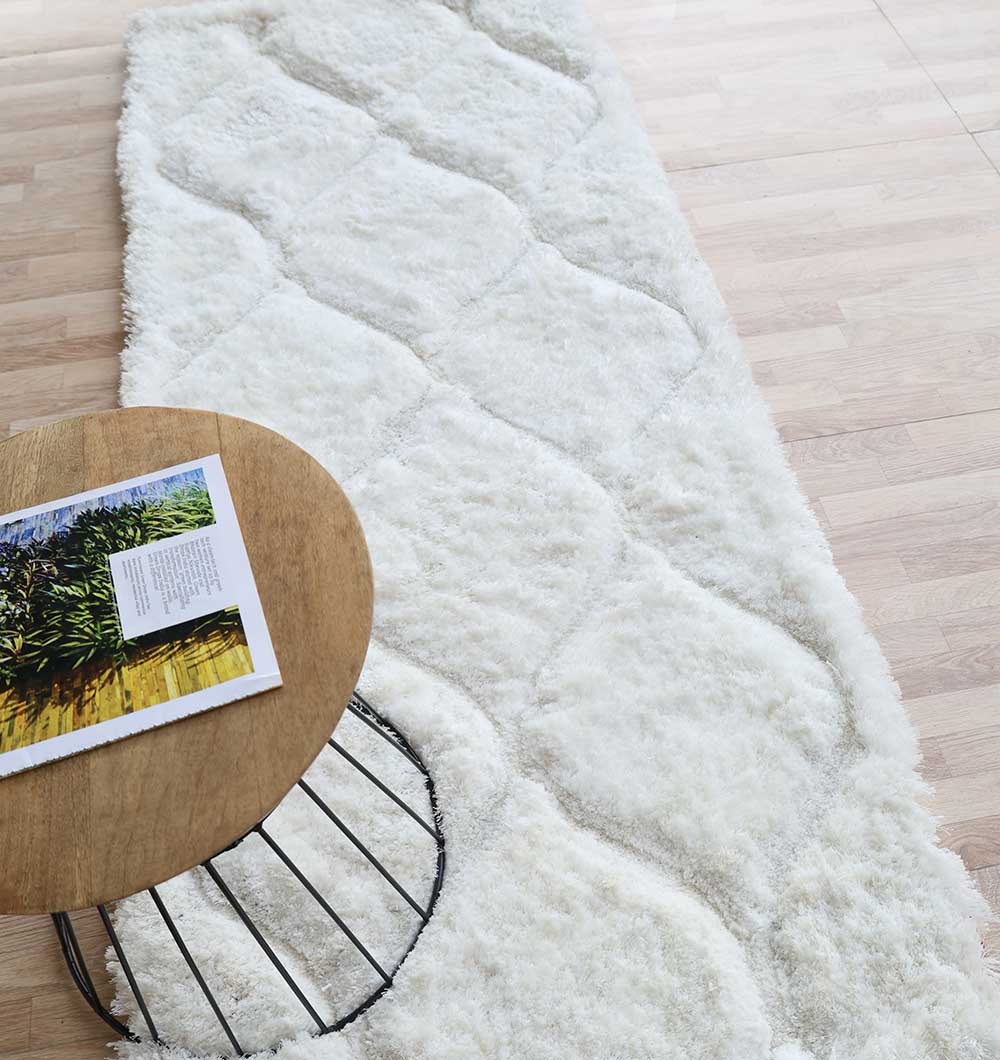 The RAMSHA HOME White Rectangle Shaggy Rug with Carved Diamond Pattern - MP3D 13 features a plush pile and lies on a light wood floor beside a round wooden table with an open magazine.