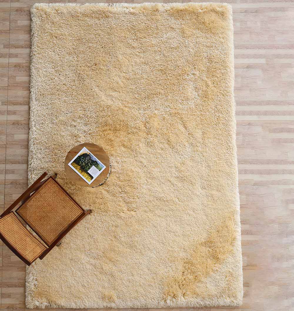 The Handmade Fluffy Shaggy Rug, Cream Color - MPV 08 is shown on a wooden floor with a wooden chair and a round side table in the corner, holding a book and small plant.