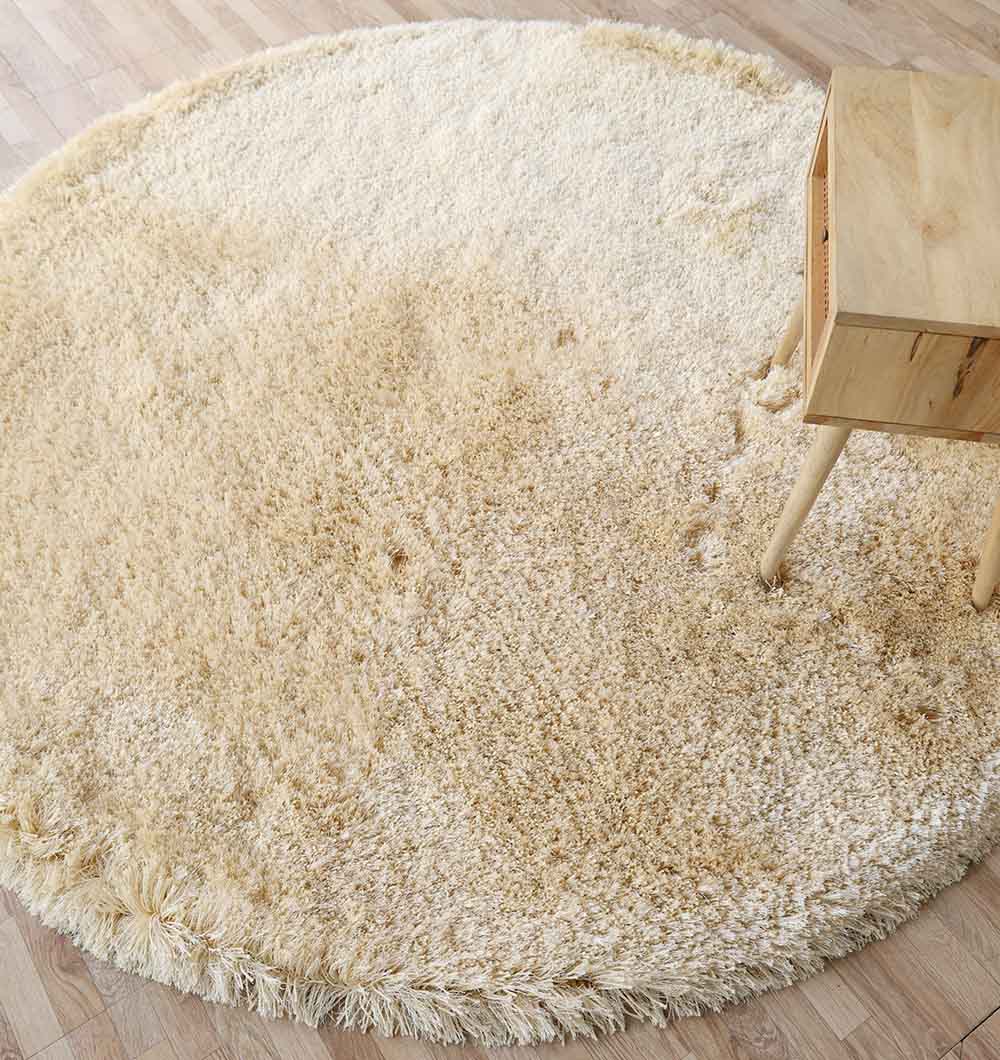 The Handmade Fluffy Shaggy Rug, Cream Color - MPV 08 lies on a wooden floor, its plush cream shag visible beneath one leg of a small light wood table near the rug’s edge.