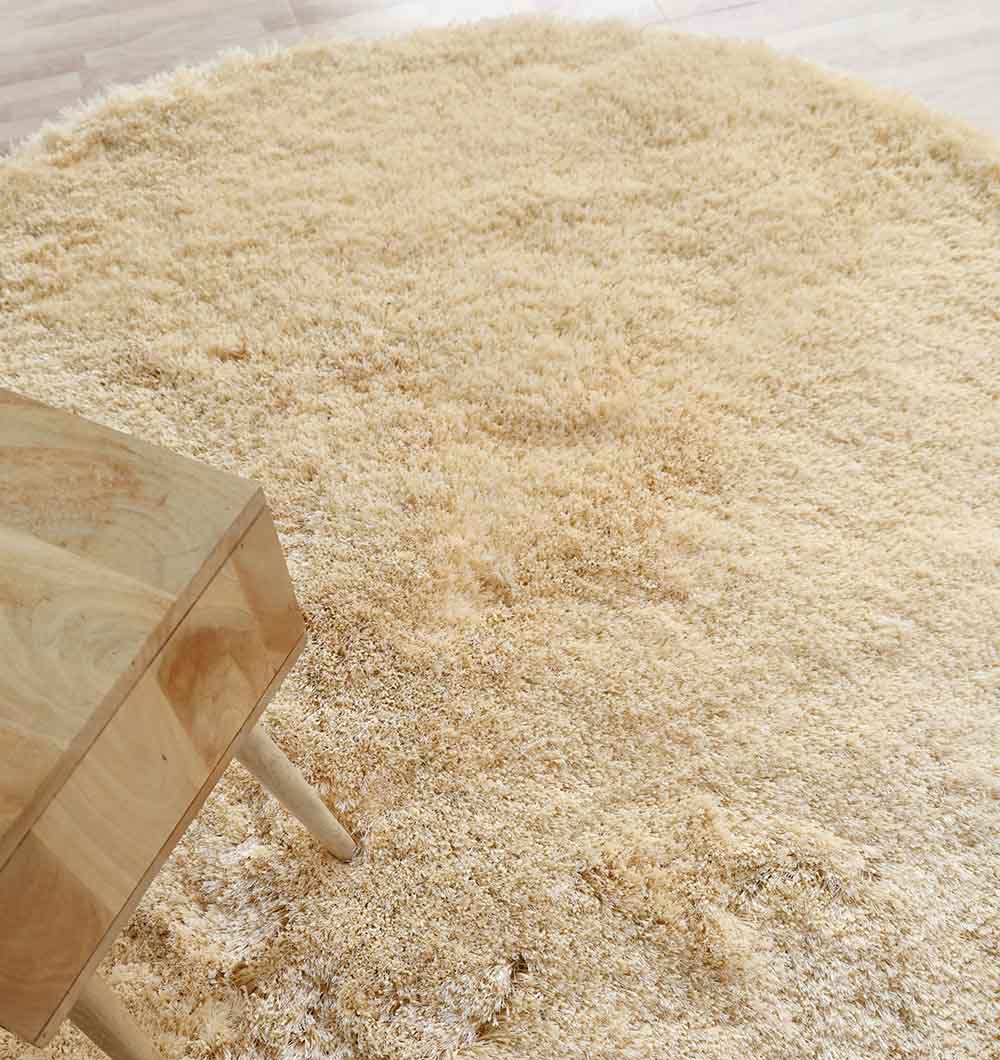 A close-up of the Handmade Fluffy Shaggy Rug in cream (MPV 08) on a wooden floor, with a light wooden table in the upper left corner, highlights the rug’s cozy and plush texture.