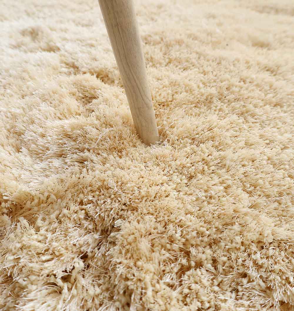 A close-up of a wooden stick pressing into the Handmade Fluffy Shaggy Rug, Cream Color - MPV 08, highlights its thick, soft, and textured fibers.
