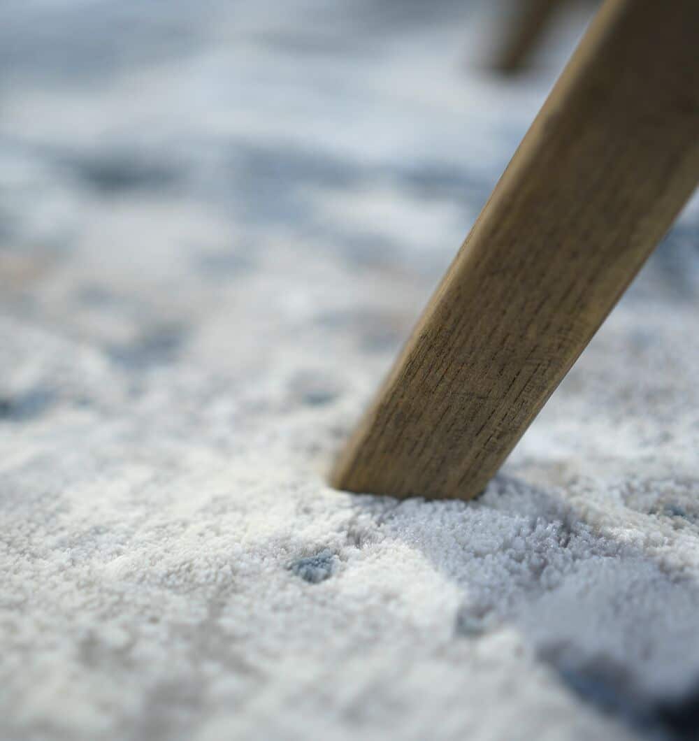 Close-up of a wooden furniture leg pressing into the soft, textured surface of the RAMSHA HOME Machine Made Turkish Rug - MR112 FLORENCE, highlighting the contact point against its light-toned distressed pattern.