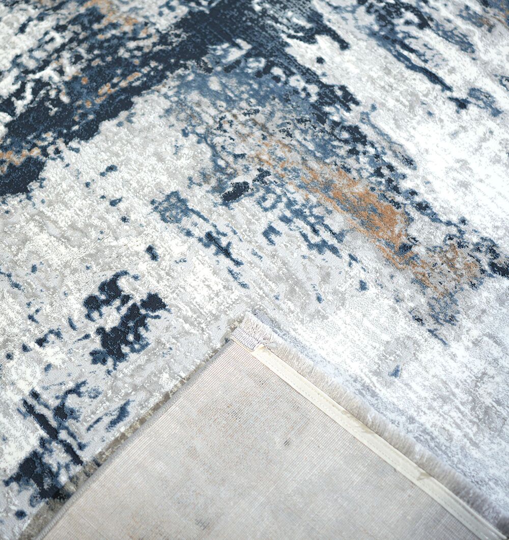The RAMSHA HOME Machine Made Turkish Rug - MR112 FLORENCE features a modern abstract design in blue, gray, white, and beige; one corner is flipped to display the plain fabric backing and stitching details.