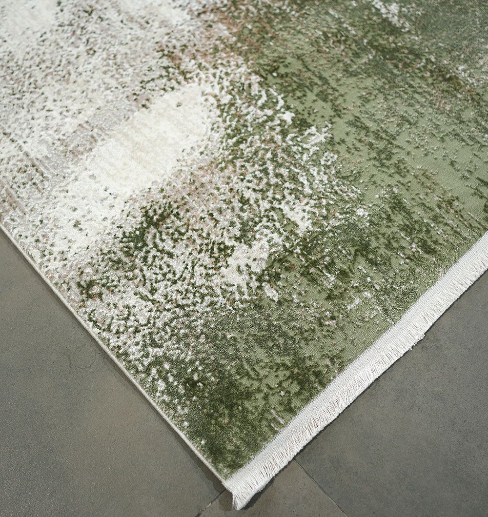 A close-up of the RAMSHA HOME Cream Green Machine Made Turkish Rug - MR165 FLORENCE shows its distressed abstract sage green and white pattern with white fringe, lying on a gray tile floor.