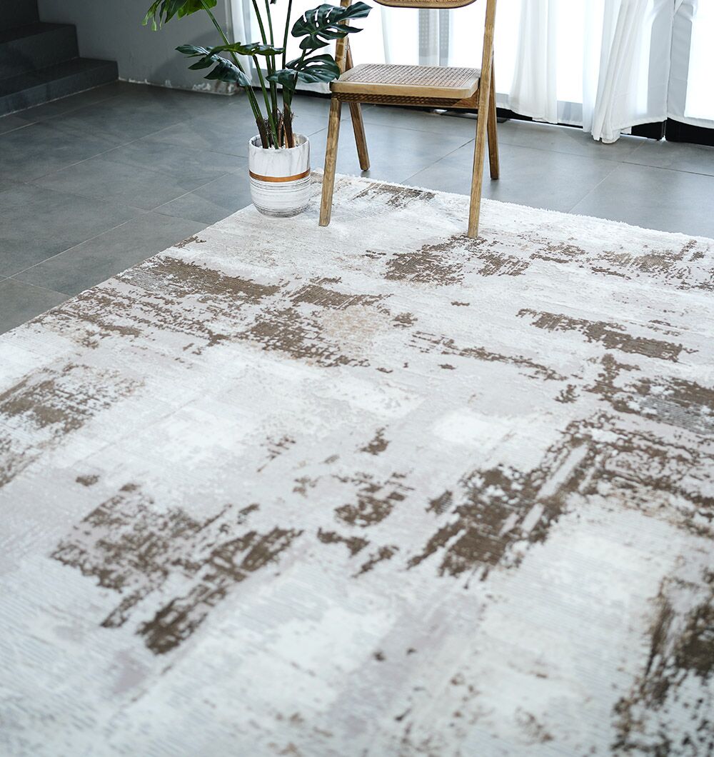 A modern room with gray tile flooring, the RAMSHA HOME MR167 FLORENCE Turkish area rug in beige and brown, a wooden chair with woven seat, a potted plant, and sheer white curtains letting in natural light.