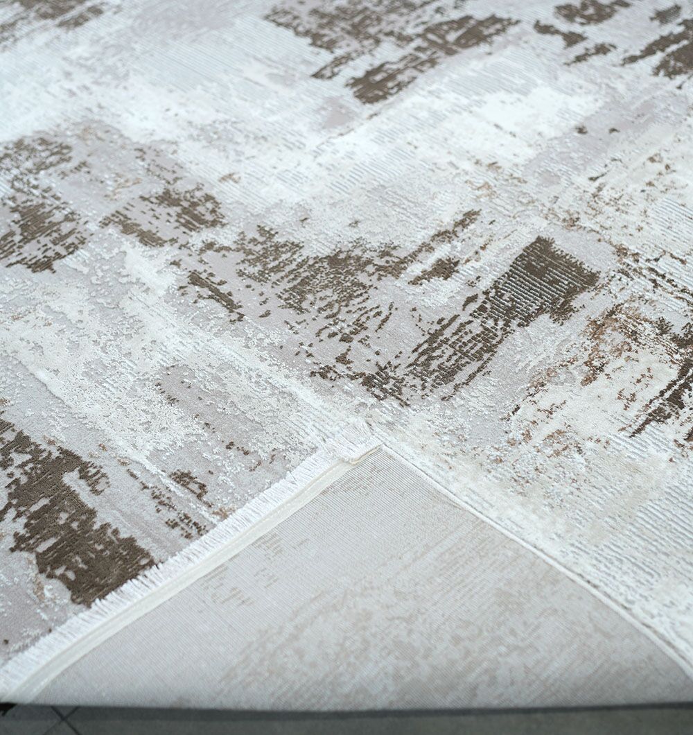 A close-up of the RAMSHA HOME MR167 FLORENCE Turkish area rug shows its modern abstract beige, cream, and brown pattern. One corner is folded, highlighting the textured surface and underside.