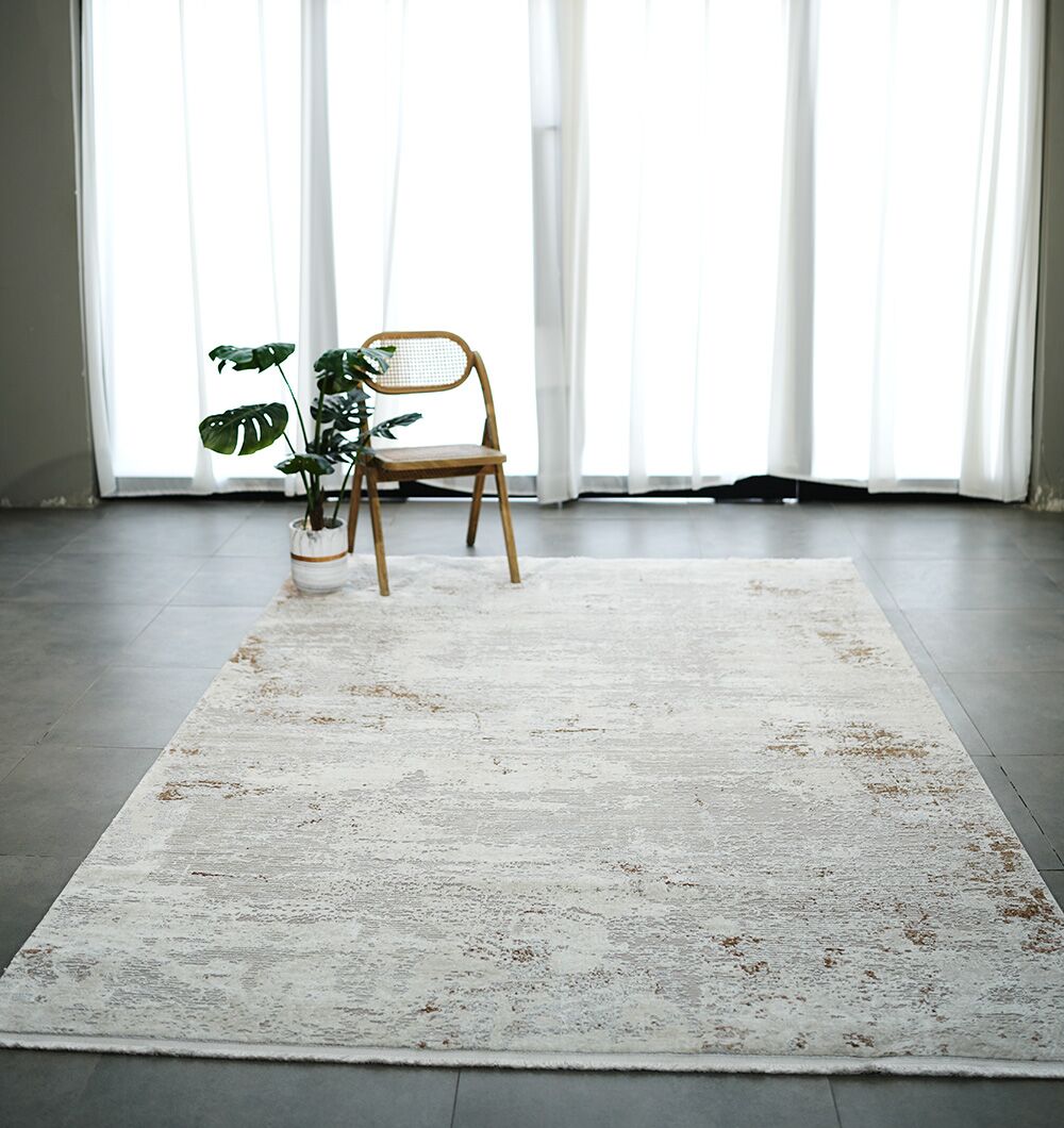 A minimalist room with sheer white curtains, a RAMSHA HOME Cream Gold Machine Made Turkish Rug (MR172 FLORENCE), a wooden chair, and a potted plant on tiled floors. Natural light fills the space.