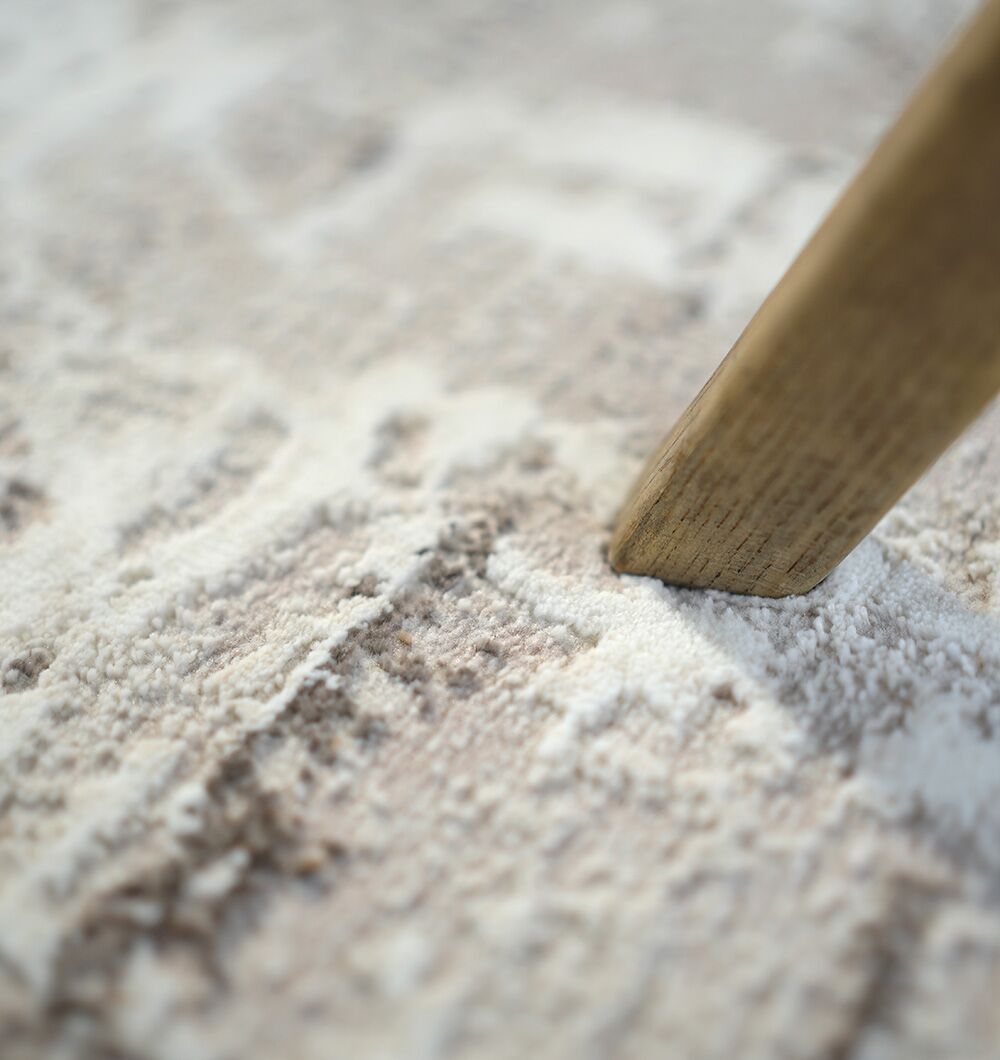 A close-up of a wooden furniture leg on the D.Vizon Gold Machine Made Turkish Area Rug - MR267 FLORENCE by RAMSHA HOME, showcasing the beige and cream patterned texture of both the rug and the wood grain.