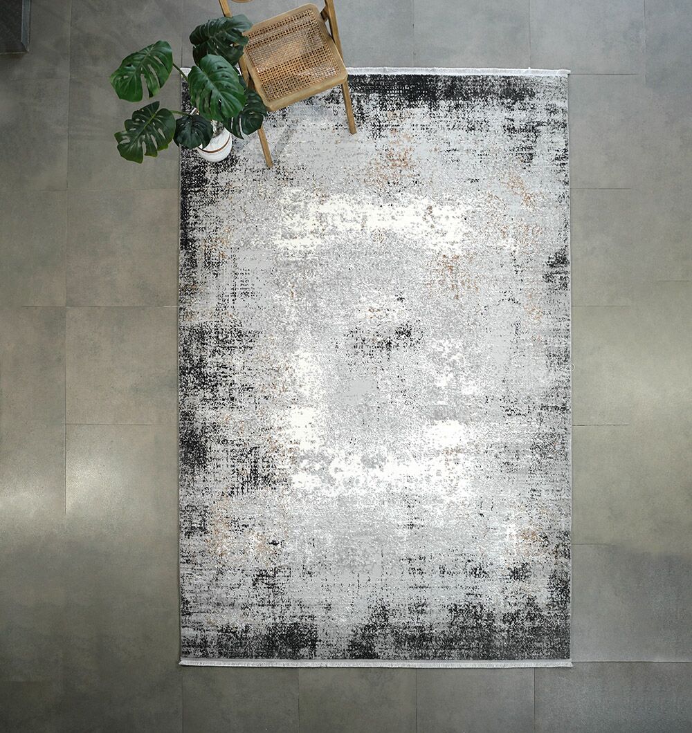 Overhead view of the RAMSHA HOME Machine Made Turkish Area Rug - MR529 FLORENCE, featuring distressed gray, black, and white tones on a tiled floor, complemented by a wooden chair and a potted plant in the corner.