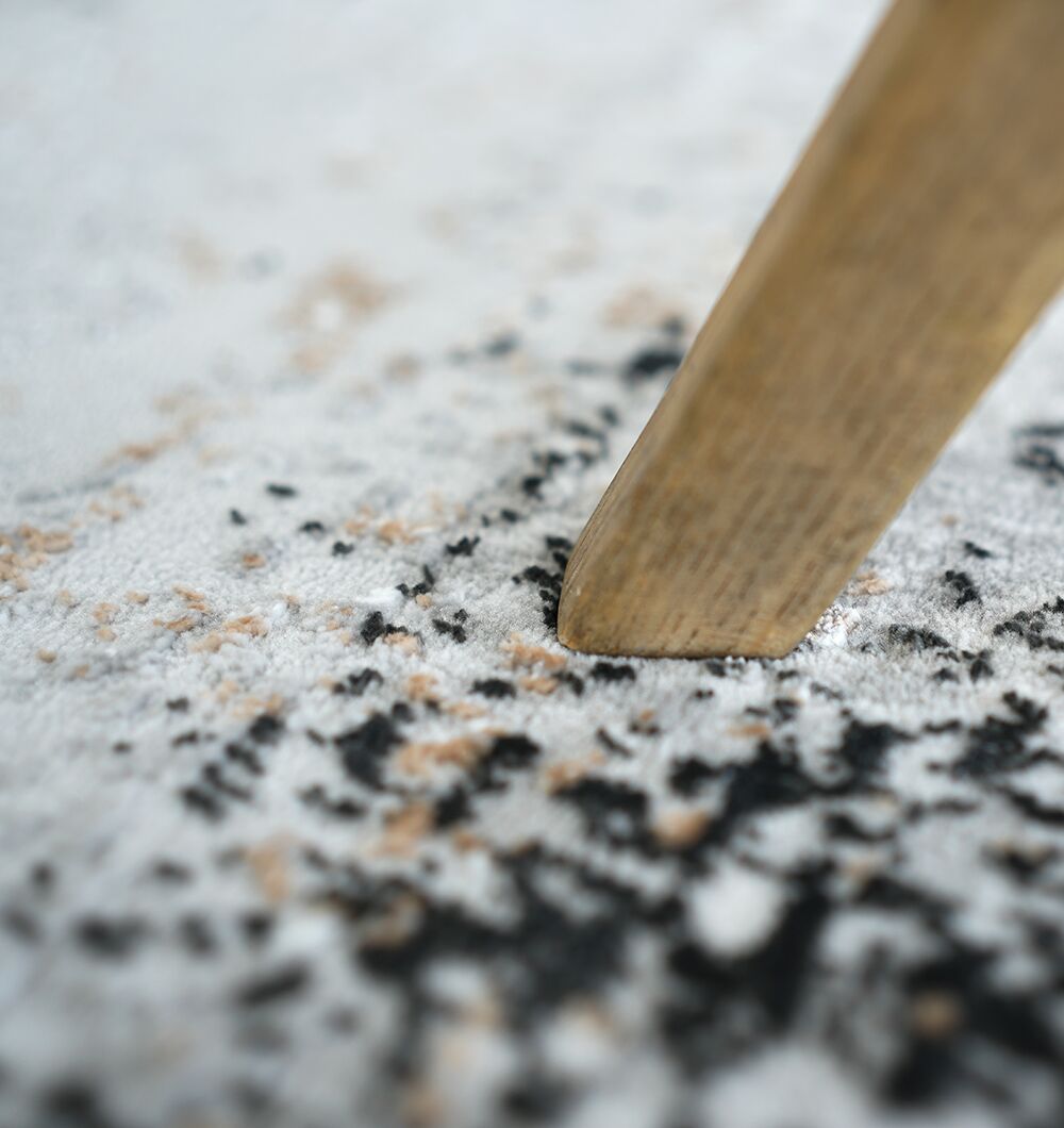 A close-up of a wooden furniture leg resting on the RAMSHA HOME Machine Made Turkish Area Rug - MR529 FLORENCE, featuring a white, black, and beige pattern.