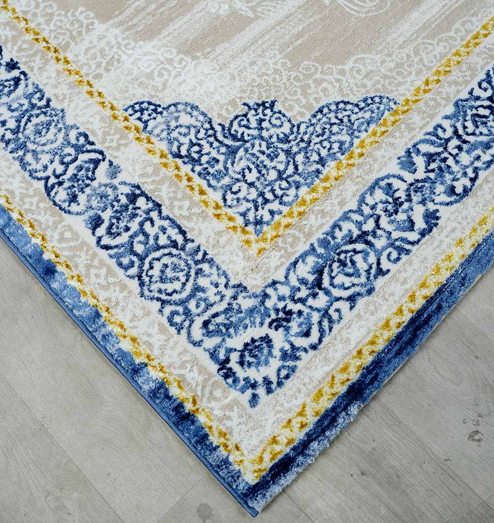 A close-up of the RAMSHA HOME Machine Made Turkish Area Rug - N370A MADRID, featuring ornate blue and yellow borders, displayed on a light gray wooden floor.