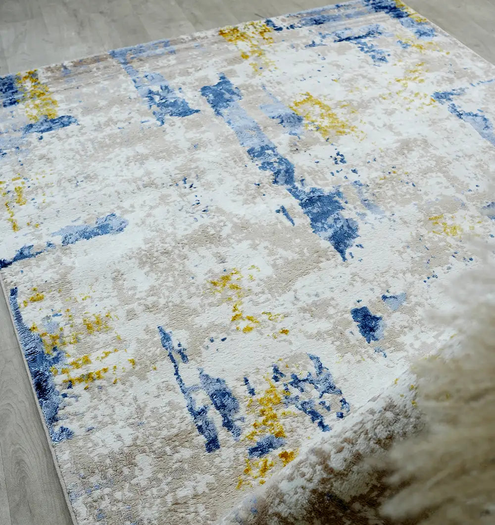 The RAMSHA HOME Machine Made Turkish Area Rug - N371A MADRID, featuring an abstract blue, yellow, and beige design, adds a modern artistic touch to the light wood floor—perfect for a modern industrial style.