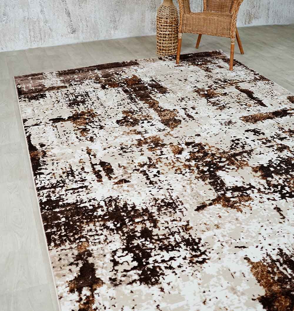 The RAMSHA HOME Beige & Dark Brown Turkish Area Rug (N371B MADRID) lies on a light wooden floor, enhanced by a wicker chair and vase near a textured wall, bringing modern style to the space.
