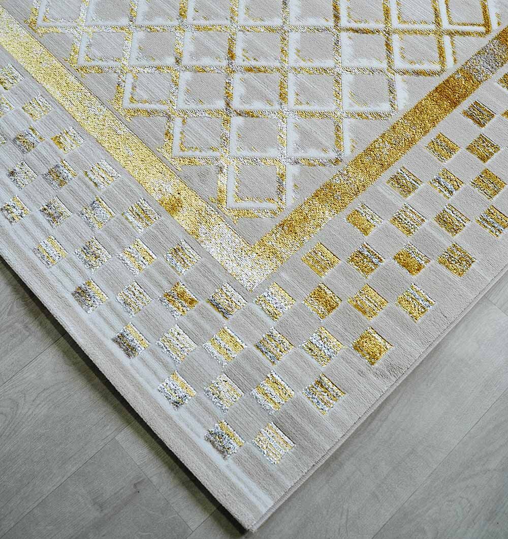 A close-up of the RAMSHA HOME Beige & Gold Silk-Feel Turkish Rug - NK71A MADRID, featuring a light hue with a gold geometric border pattern, shown on a light wood floor.