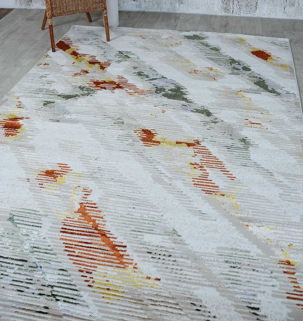 The RAMSHA HOME Machine Made Turkish Decor Rug - NK73A MADRID features abstract diagonal streaks in orange, green, and yellow on a light base. It’s shown on a light wood floor beside a wicker chair and a textured wall.