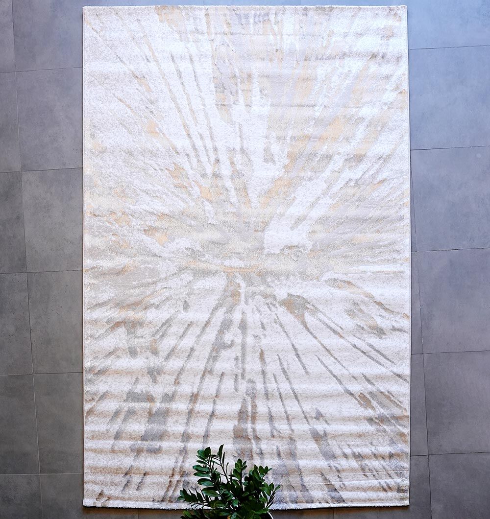 The RAMSHA HOME Abstract Sunburst Machine Made Turkish Decor Rug - NK79A MADRID, featuring a light beige and gray burst pattern, lies on a gray tiled floor with a small green leafy plant at its bottom edge.