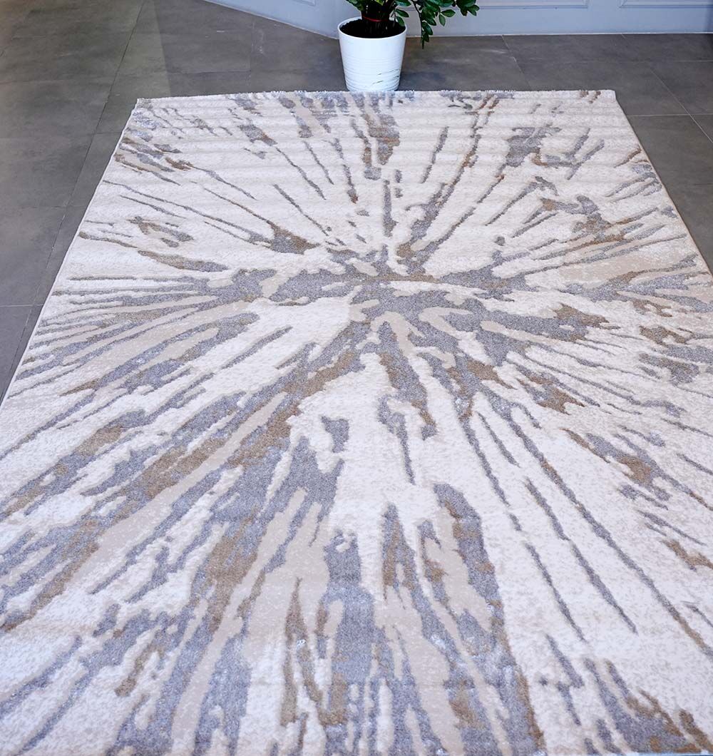 The RAMSHA HOME Abstract Sunburst Machine Made Turkish Decor Rug - NK79A MADRID features a rectangular shape with a radiating beige, gray, and tan pattern. A potted plant in a white pot sits at the rug’s top edge on tiled flooring.