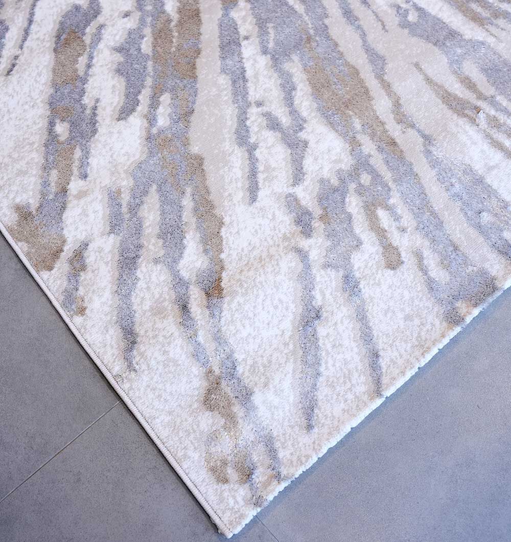 A close-up of the RAMSHA HOME Abstract Sunburst Machine Made Turkish Decor Rug - NK79A MADRID, featuring an abstract pattern in light beige, gray, and white tones, displayed on a smooth, light-colored tiled floor.